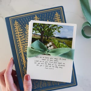 May include: A white card with a green ribbon tied around it. The card features a watercolor painting of a tree and a field. The text on the card reads: "Make me to know your ways, O Lord: teach me your paths. Lead me in your truth and teach me, for you are the God of my salvation; for you I wait all the day long. Psalm 25:4-5"