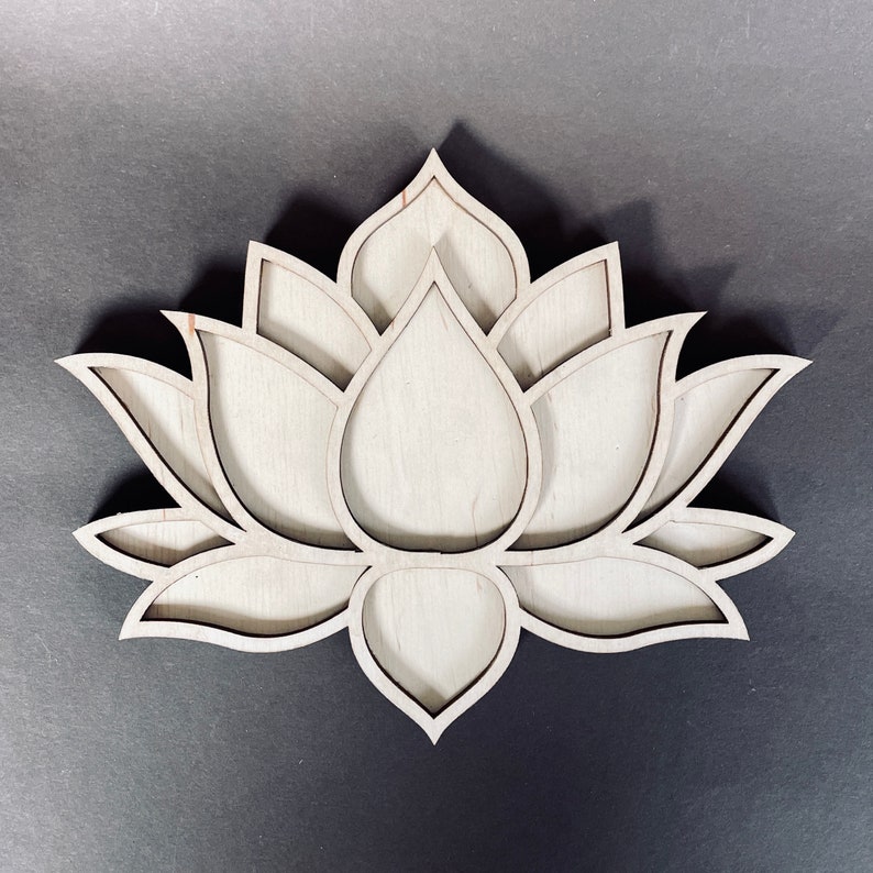 May include: A wooden lotus flower design with intricate details and a layered effect. The design is cut out of a single piece of wood and has a natural wood finish.