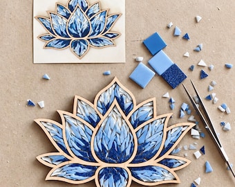 May include: A lotus flower mosaic craft project featuring a wooden frame filled with various shades of blue and white glass tiles. The set includes a finished lotus piece, a template, loose glass tiles, and a pair of metal tweezers.
