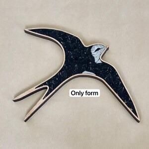 May include: A black and white mosaic bird sculpture in the shape of a swallow. The bird is made of small pieces of glass and is mounted on a wooden base.