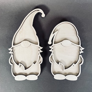 May include: Two unfinished wooden gnome ornaments with a beard and hat design. The gnomes are standing upright and are ready to be painted.