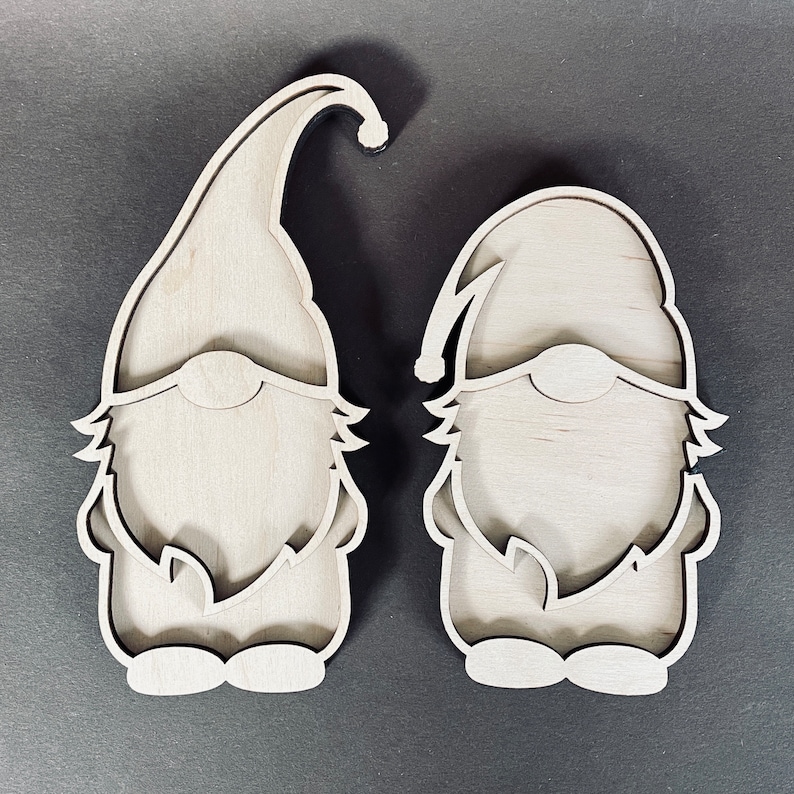 May include: Two unfinished wooden gnome ornaments with a beard and hat design. The gnomes are standing upright and are ready to be painted.
