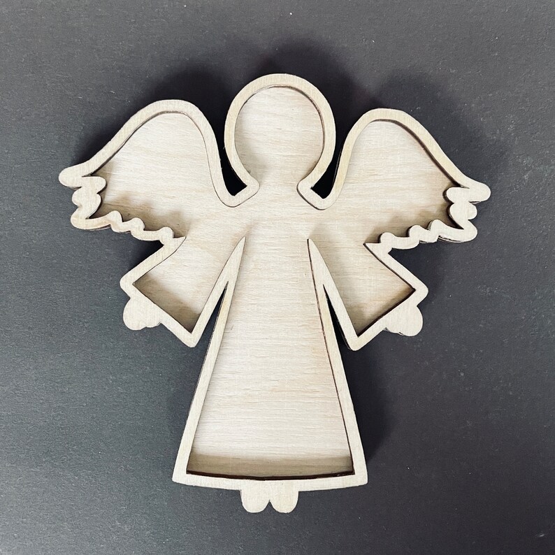 May include: Wooden cutout of an angel with wings, a halo, and a dress. The cutout is unfinished and ready to be painted or decorated.