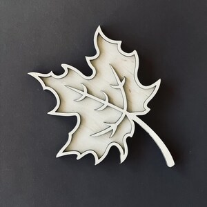 May include: A white wooden maple leaf cutout with a detailed vein pattern. The leaf is a simple, elegant design that would look great in a home decor setting.