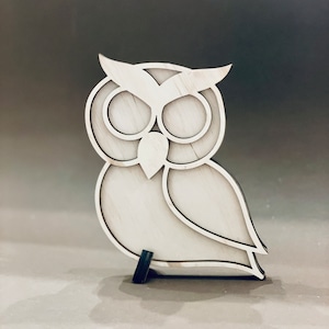 May include: A white wooden owl figurine with a detailed design. The owl has large eyes and a beak. The figurine is standing on a small black base.