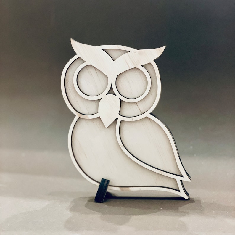 May include: A white wooden owl figurine with a detailed design. The owl has large eyes and a beak. The figurine is standing on a small black base.