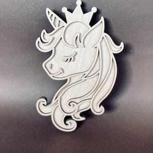 May include: A wooden cutout of a unicorn head with a crown. The unicorn has closed eyes and a detailed mane.