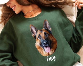 May include: Dark green sweatshirt featuring a detailed portrait of a German Shepherd dog with its tongue out. The dog's name, "Lucy", is written in white script below the image. The sweatshirt is a solid color.