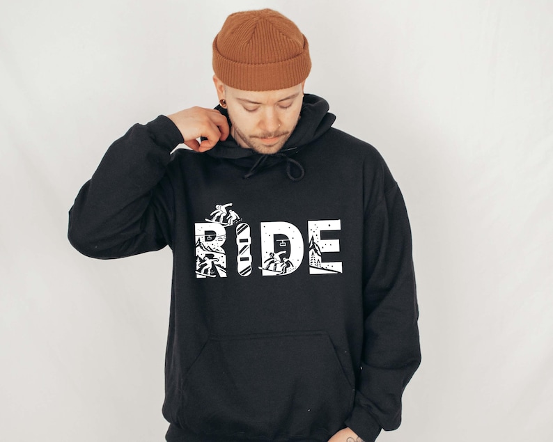 May include: Black hoodie with the word "RIDE" in white block letters. The letters are filled with images of skiers and snowboarders. The hoodie has a front pocket and a drawstring hood.
