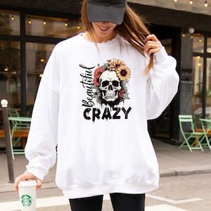 May include: White sweatshirt with a skull and flowers graphic and the text "Beautiful Crazy".