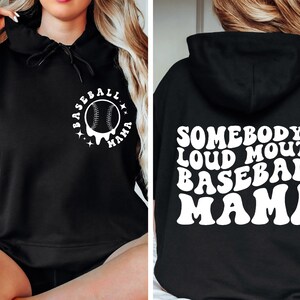 Op de afbeelding: Zwarte hoodie met witte tekst en honkbalafbeelding. De voorkant heeft een honkbalafbeelding met de woorden "Baseball Mama". De achterkant van de hoodie zegt "Somebody's Loud Mouth Baseball Mama".