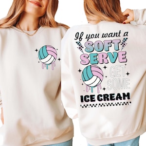 May include: A cream-colored sweatshirt with a volleyball graphic and the text "If you want a soft serve get some ice cream" on the back. The volleyball graphic is pink, blue, and white with a dripping effect. The text is in black with a pink and blue outline.