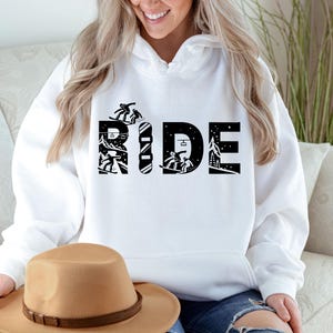 May include: White hoodie with the word "RIDE" in large black letters. The letters are designed with snowboarders and a snowboard. The hoodie is a comfortable, casual style.