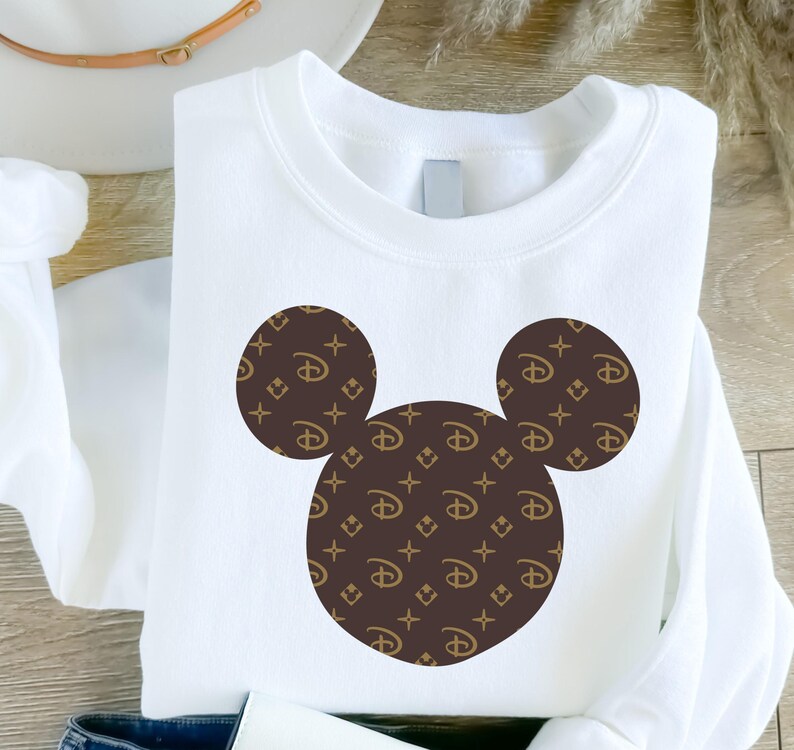 Puede incluir: Sudadera blanca con un dise&ntilde;o de Mickey Mouse. La silueta de Mickey Mouse est&aacute; compuesta por tres c&iacute;rculos marrones, cada uno lleno con un patr&oacute;n repetido del logotipo de Disney y un logotipo 'LV' estilizado.