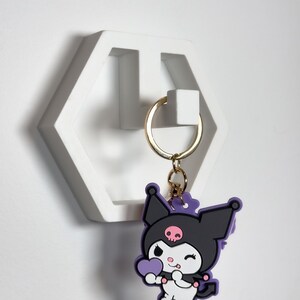 May include: White hexagonal wall hook with a gold key ring and a purple and black Hello Kitty keychain with a pink heart.