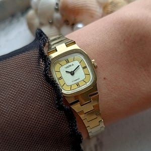 Pu&ograve; includere: Un orologio da polso vintage color oro con quadrante rettangolare. Il quadrante &egrave; color crema chiaro con lancette nere e numeri romani. Il cinturino &egrave; in tinta oro.