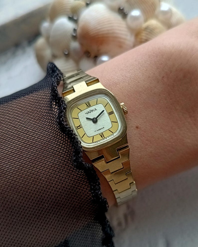 Pu&ograve; includere: Un orologio da polso vintage color oro con quadrante rettangolare. Il quadrante &egrave; color crema chiaro con lancette nere e numeri romani. Il cinturino &egrave; in tinta oro.
