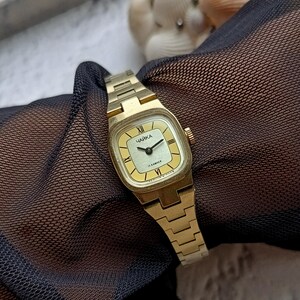 Pu&ograve; includere: Un orologio da polso vintage color oro con quadrante quadrato e cinturino abbinato. Il quadrante &egrave; giallo chiaro con lancette nere e numeri romani. La parola "ЧАЙКА" &egrave; stampata sul quadrante.