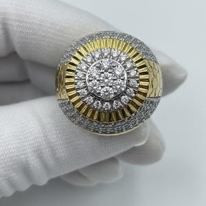 Peut inclure: Une grosse bague ronde avec un design or et argent. Le centre présente un groupe de petites pierres claires entourées de cercles concentriques d'or et d'argent. La bande est incrustée de pierres plus petites.