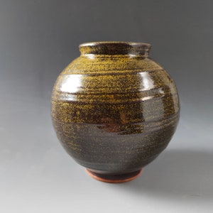 May include: A round, dark brown ceramic vase with a speckled, yellow glaze. The vase has a wide base and a narrow opening.