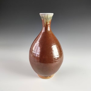 Könnte beinhalten: Eine braune Keramikvase mit weißem Rand und glänzender Oberfläche. Die Vase hat einen runden Körper und einen schmalen Hals.