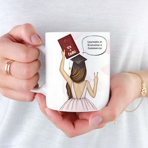 Op de afbeelding: Witte keramische mok met een cartoonillustratie van een vrouw die een afstudeerhoed draagt en een boek vasthoudt waarop "TESI di Giulia" staat. De spreekballon zegt "Laureata in Economia e Commercio".