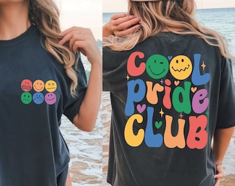 Puede incluir: Una camiseta negra con un gráfico de arcoíris en la espalda que dice "Cool Pride Club". La parte delantera de la camiseta tiene un arcoíris de caras sonrientes.