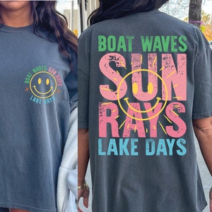 Op de afbeelding: Een oversized donkergrijs T-shirt met een grafische print van een smiley en de tekst "Boat Waves Sun Rays Lake Days". De grafiek is in roze, geel, groen en blauw.