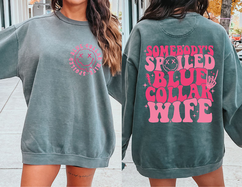 May include: A dark green sweatshirt with a pink graphic that says "Somebody's Spoiled Blue Collar Wife" with a smiley face and a skeleton hand.