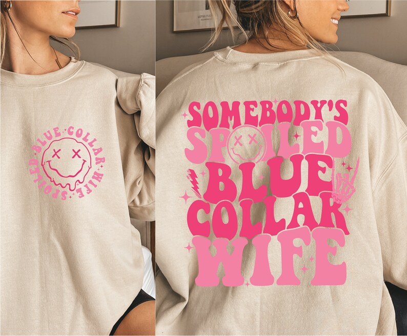 May include: A light beige sweatshirt with a pink graphic on the back that says "Somebody's Spoiled Blue Collar Wife" and a pink graphic on the front that says "Somebody's Spoiled Blue Collar Wife" with a smiley face.