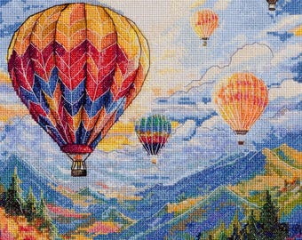 Könnte beinhalten: Ein Kreuzstich-Landschaftsbild zeigt Heißluftballons, die über einer Bergkette schweben. Der größte Ballon ist eine lebendige Mischung aus Rot, Orange und Gelb. Andere Ballons sind orange und grün. Der Himmel ist blau mit Wolken, und die Berge sind blau und lila.