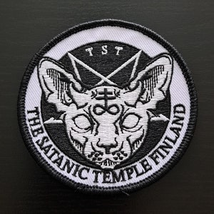 May include: Black and white embroidered patch featuring a cat's head, a pentagram, and the text "The Satanic Temple Finland" around the edge.
