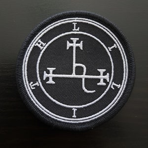 May include: A black and white embroidered patch featuring a sigil, a symbol of a demon, enclosed within a circle with letters. The sigil is a cross with a curved line at the bottom.