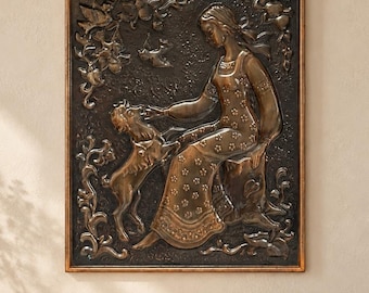 May include: A rectangular bronze-toned metal wall plaque featuring a relief sculpture of a person sitting on a tree stump, interacting with a small dog. The scene is surrounded by embossed floral and foliage details within a simple wooden frame.