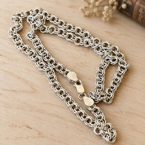 May include: A silver-toned chain necklace featuring a complex, interlocking circular link design. The necklace is constructed with a repeating pattern of small, connected rings and includes a secure lobster claw clasp mechanism at the center.