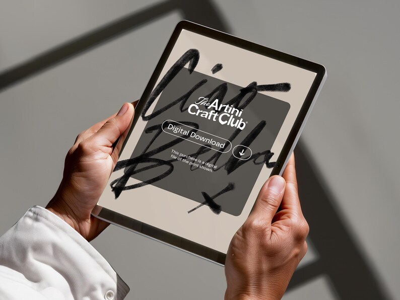 K&ouml;nnte beinhalten: Ein digitales Tablet, das einen digitalen Download vom The Artini Craft Club anzeigt. Der Bildschirm zeigt ein dunkelgraues Rechteck mit wei&szlig;em Text und einem Pfeil nach unten. Das Tablet wird von zwei H&auml;nden vor einem neutralen Hintergrund gehalten.