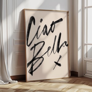 K&ouml;nnte beinhalten: Ein gerahmter Kunstdruck mit den Worten "Ciao Bella" in schwarzer Schrift auf cremefarbenem Hintergrund. Das Kunstwerk wird in einem Raum mit nat&uuml;rlichem Licht pr&auml;sentiert und lehnt an einer Wand. Der Rahmen ist goldfarben.