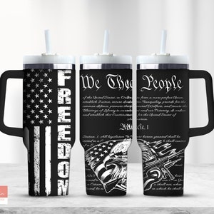Op de afbeelding: Een zwart-witte beker met een handvat en een rietje. De beker heeft een verweerd Amerikaans vlagontwerp met het woord "FREEDOM" dat verticaal aan de rechterkant is gedrukt. De andere kant van de beker heeft de tekst "We The People" uit de preambule van de Amerikaanse Grondwet.