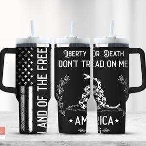 Op de afbeelding: Drie zwart-witte roestvrijstalen bekers met deksels en handvatten. De bekers hebben een patriottisch ontwerp met een Amerikaanse vlag, een slang en de tekst "Land of the Free", "Liberty or Death", "Don't Tread on Me" en "America".