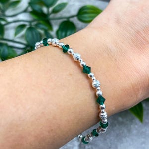 Könnte beinhalten: Ein silbernes Armband mit abwechselnd facettierten smaragdgrünen Perlen und strukturierten silbernen Perlen. Das Armband ist auf einer flexiblen Schnur aufgefädelt. Das Armband wird an einem Handgelenk gezeigt.