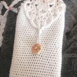 May include: White crocheted phone case with a floral button and a crocheted strap.