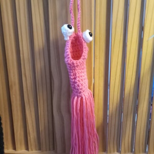 May include: A pink crocheted octopus with white googly eyes hanging from a wooden surface.