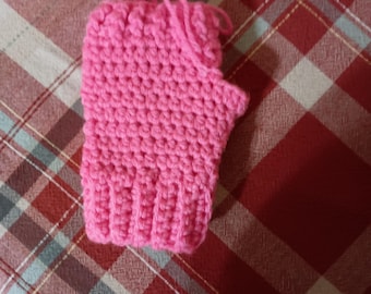 Op de afbeelding: Een felroze vingerloze handschoen gemaakt met een gehaakt textuurpatroon. De handschoen heeft een geribbelde boord bij de pols en een opening voor de duim, met losse garendraden zichtbaar aan de bovenrand van het handgedeelte.