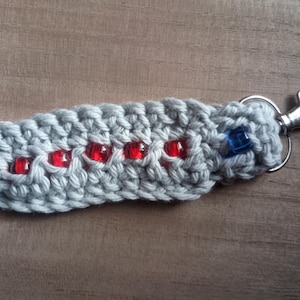 May include: Gray crocheted keychain with red and blue beads and a silver key ring.