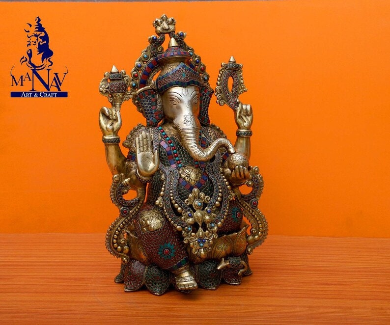 Puede incluir: Una estatua dorada de Ganesha con intrincados detalles y piedras preciosas de colores. La estatua est&aacute; sentada sobre una base de loto y tiene la trompa girada hacia la izquierda.