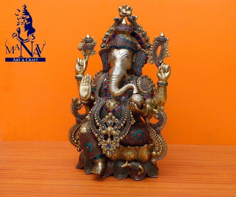 Puede incluir: Una estatua dorada de Ganesha, el dios hind&uacute; de la sabidur&iacute;a y la prosperidad, con detalles intrincados y piedras preciosas de colores. La estatua est&aacute; sentada sobre una base de loto y tiene una trompa, orejas grandes y cuatro brazos.