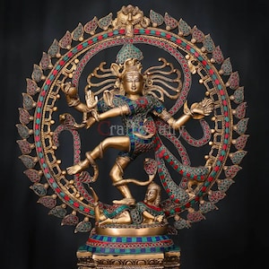 May include: A gold-toned metal sculpture of the Hindu deity Shiva in the Nataraja pose, dancing on a demon. The sculpture is adorned with colourful gemstones and intricate details. The sculpture is set on a circular base with a decorative design.