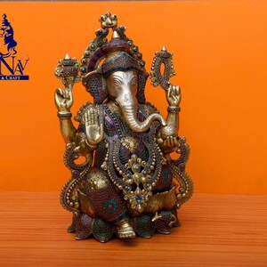 Puede incluir: Una estatua dorada de Ganesha con intrincados detalles y piedras preciosas de colores. La estatua est&aacute; sentada sobre una base de loto y tiene la trompa girada hacia la izquierda.