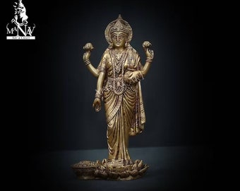 May include: A gold-colored metal statue of the Hindu goddess Lakshmi, standing on a lotus base. She is holding a lotus flower in each hand and has a gentle expression on her face.