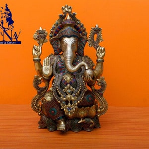 Puede incluir: Una estatua dorada de Ganesha, el dios hind&uacute; de la sabidur&iacute;a y la prosperidad, con intrincados detalles y piedras preciosas de colores. La estatua est&aacute; sentada sobre una base de loto y tiene una trompa, cuatro brazos y una corona.